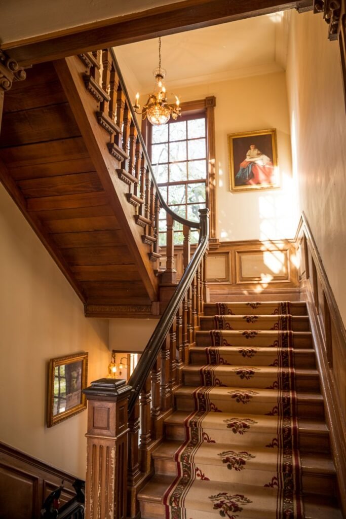 Classic wooden farmhouse stair with an ornate floral runner and detailed wooden balusters and newel post.