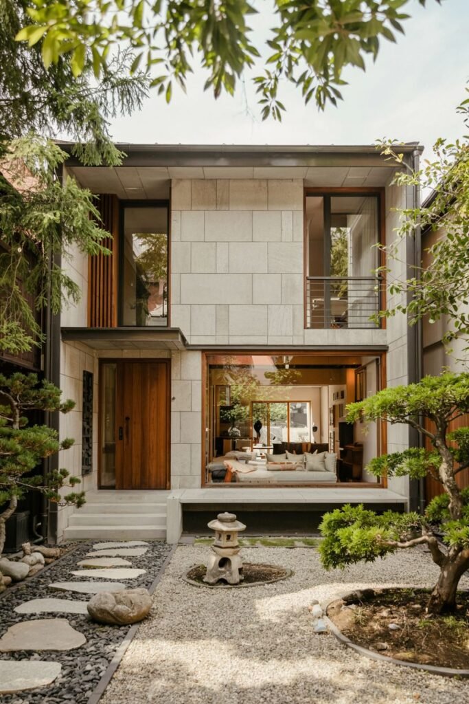 Multi-level Contemporary japandi house exterior combining light stone blocks, large glass panels, a wooden door, and a garden with stepping stones, gravel, rocks, and a traditional stone lantern.