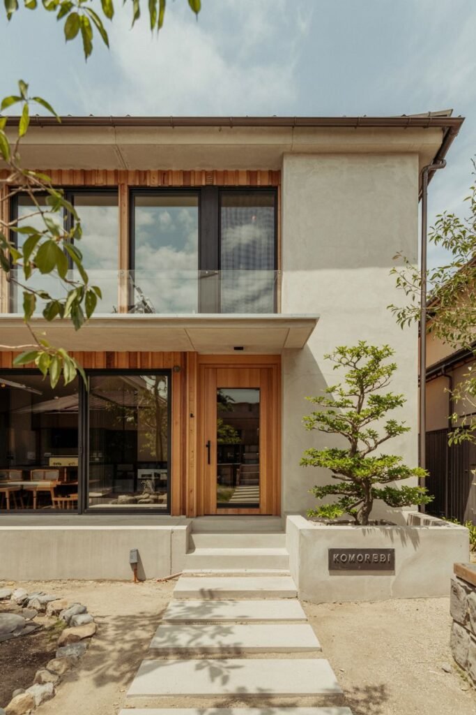 Minimalist Contemporary japandi house exterior entrance combining smooth concrete walls, warm wood siding, and a concrete planter labeled "KOMOREBI".