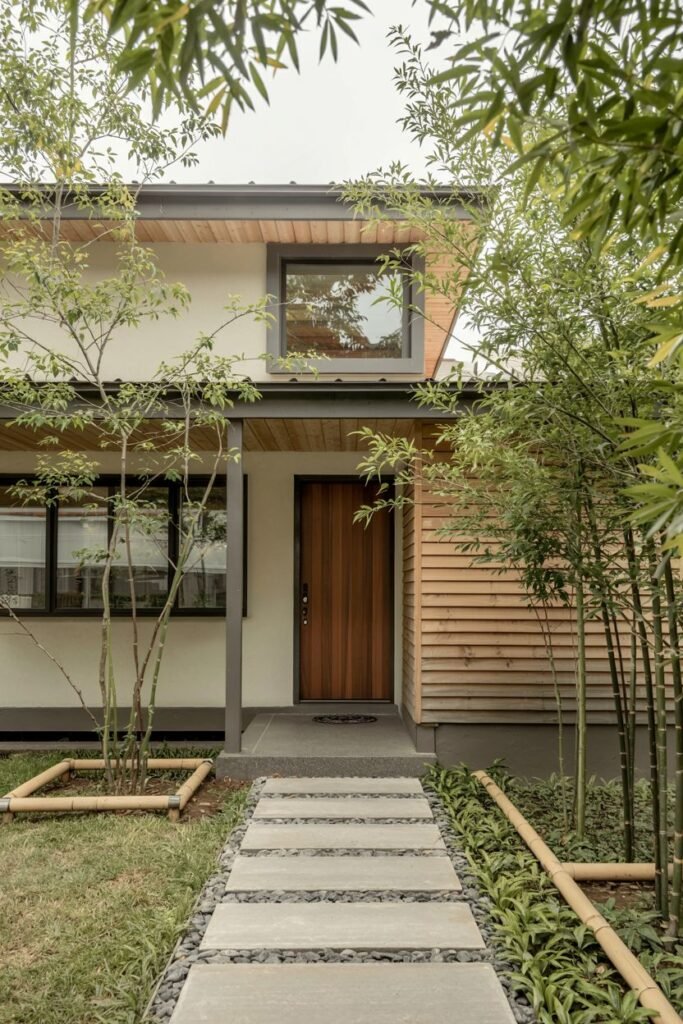 Contemporary japandi house exterior design with vertical wood siding, white walls, stepping stone path, and tall bamboo plants as landscaping elements.