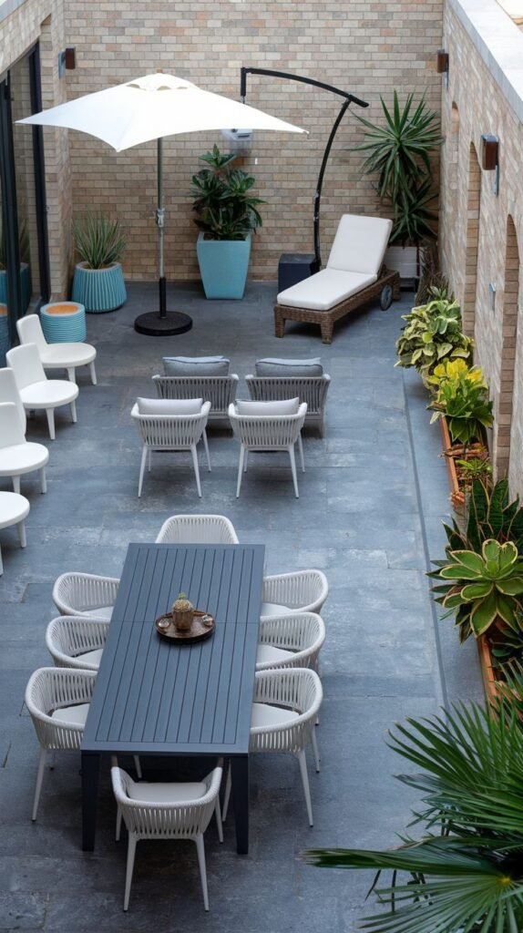 Courtyard patio with dining area, lounge chairs, and potted plants, with a large umbrella for shade.