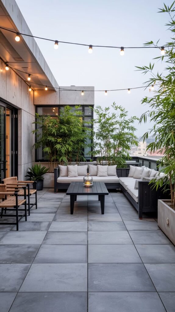 Rooftop patio with a sectional sofa, coffee table, planters with tall bamboo plants, and string lights.