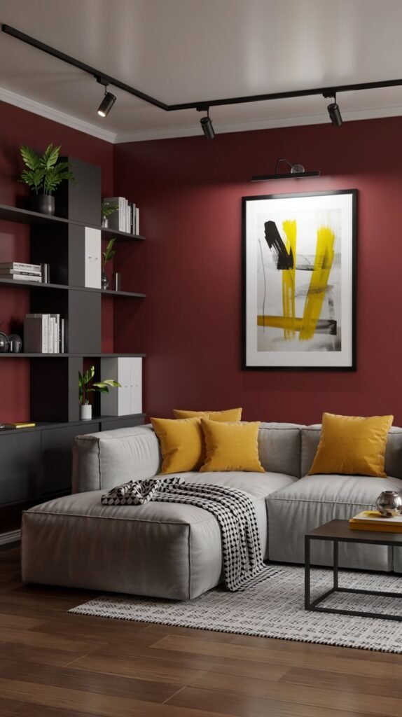 A warm living area with a gray sectional sofa with yellow pillows, a dark rug, and burgundy walls with track lighting.